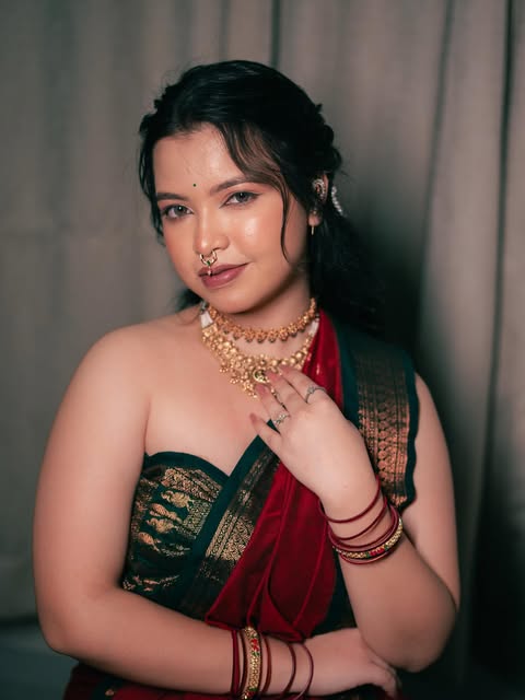 Makeup and hair portrait with a red and green sari against a muted curtain backdrop, from Pooja Salunkhe Makeover's portfolio