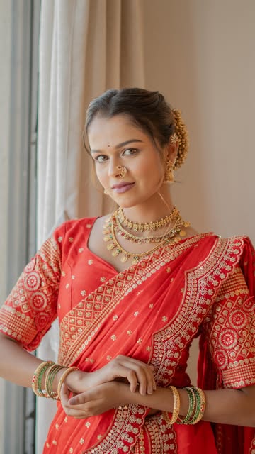 Standing portrait in a coral sari beside a window, showing makeup, jewellery and the complete styling, from Pooja Salunkhe Makeover's portfolio